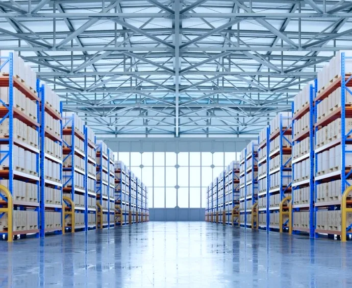 Modern distribution warehouse interior with blue metal racking systems organized in symmetrical aisles with polished concrete floors and steel truss ceiling.
