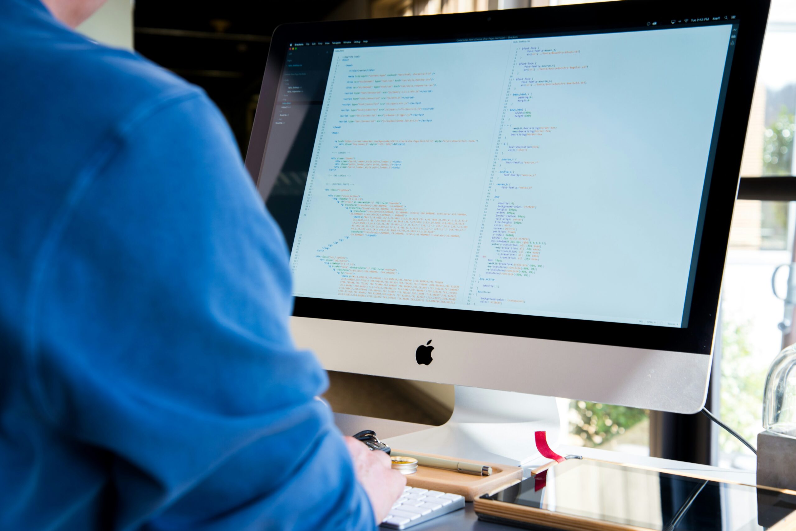 Person working on a desktop computer displaying code on a large monitor, suggesting software development or programming in progress.