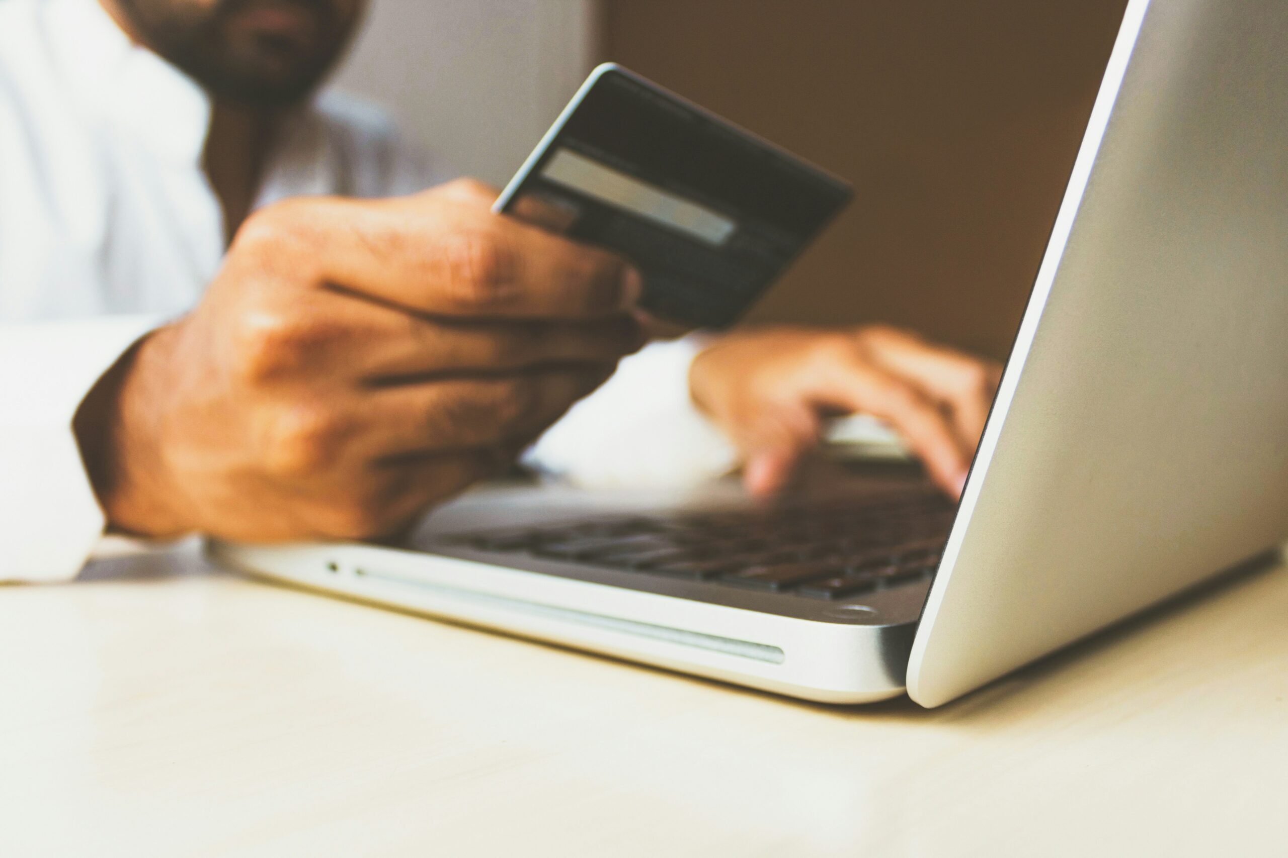 Person holding a credit card and typing on a laptop, representing online shopping or digital payment.