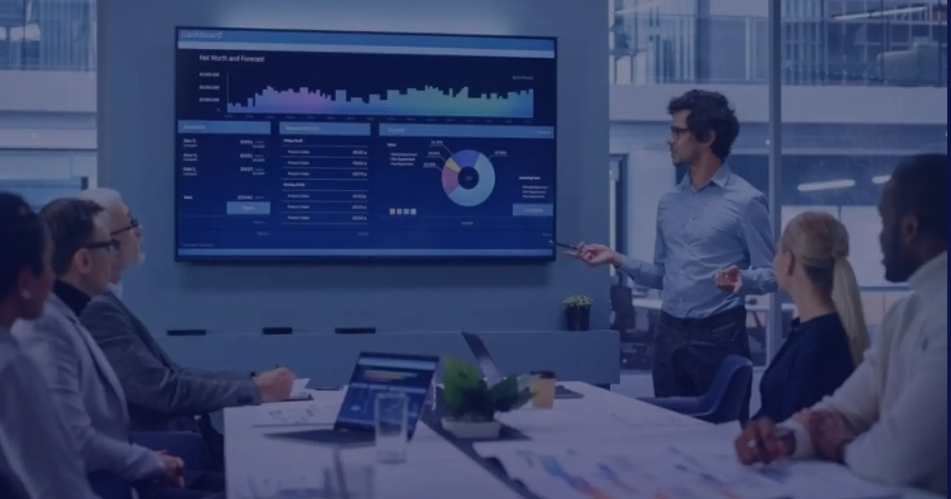 Business presentation in a modern office, man presenting analytics dashboard to a group seated at a boardroom table.