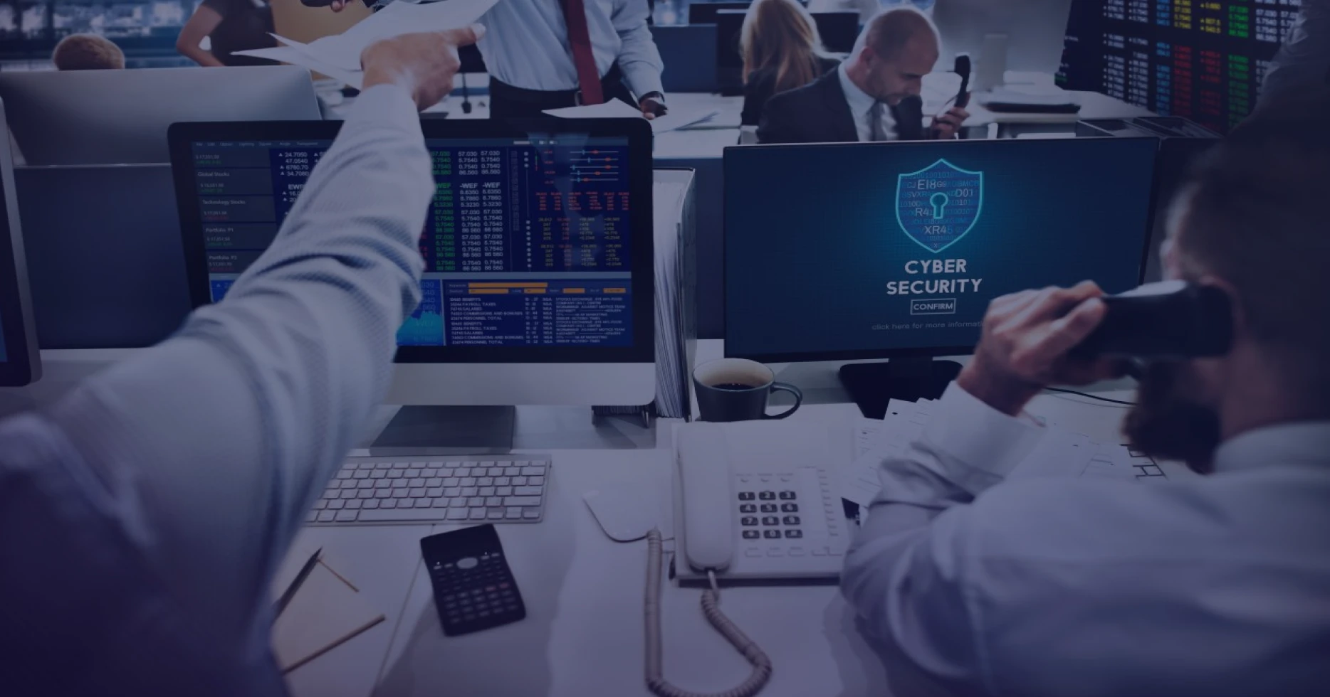 Financial professionals working with market data and cybersecurity systems in trading environment with security confirmation screen visible.